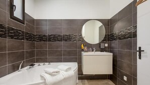 A modern bathroom with a freestanding bathtub, a round mirror, and a white vanity. - La Villa Monarque  (Agde)