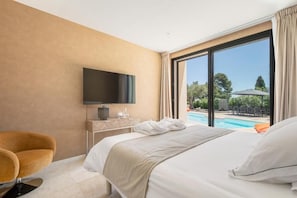 A hotel room with a bed, a TV, a chair, and a view of a swimming pool.