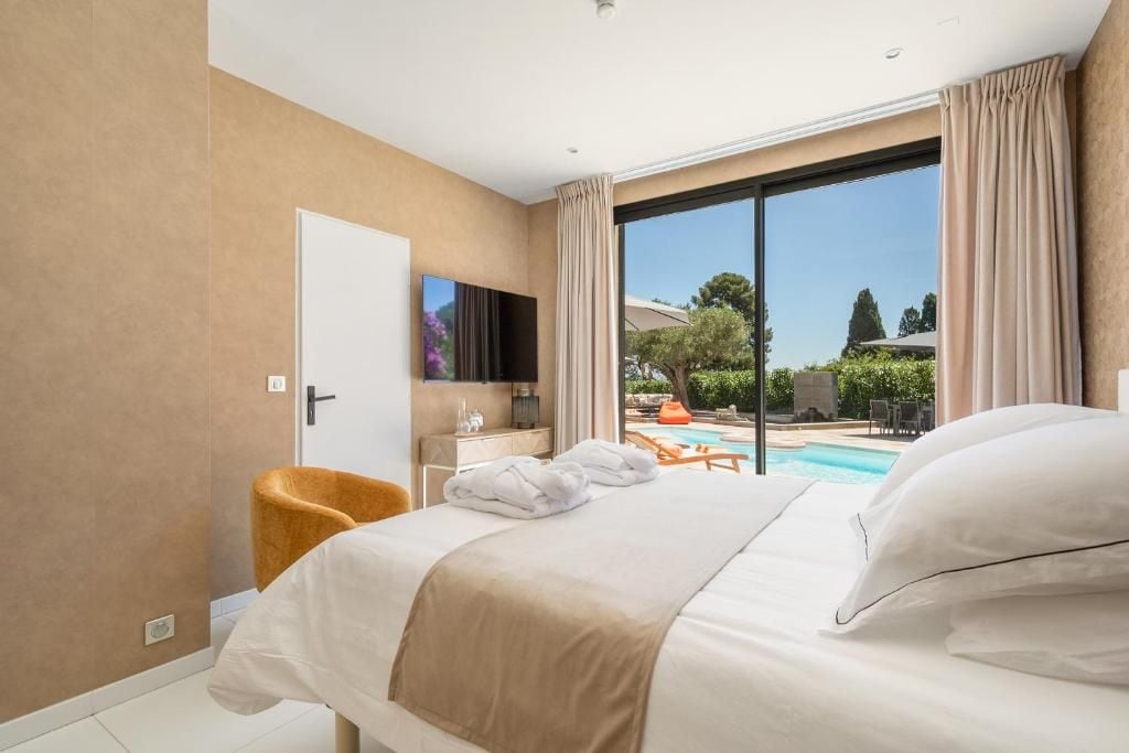 A hotel room with a bed, a TV, a desk, and a view of a swimming pool.