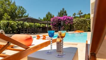 Área da piscina com espreguiçadeiras, uma mesa com duas taças e uma piscina ao fundo.