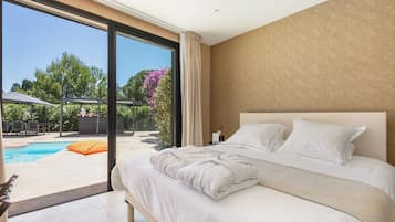 Une chambre dotée d’un grand lit, offrant une vue sur une piscine, et comprenant un patio aménagé avec du mobilier d’extérieur.