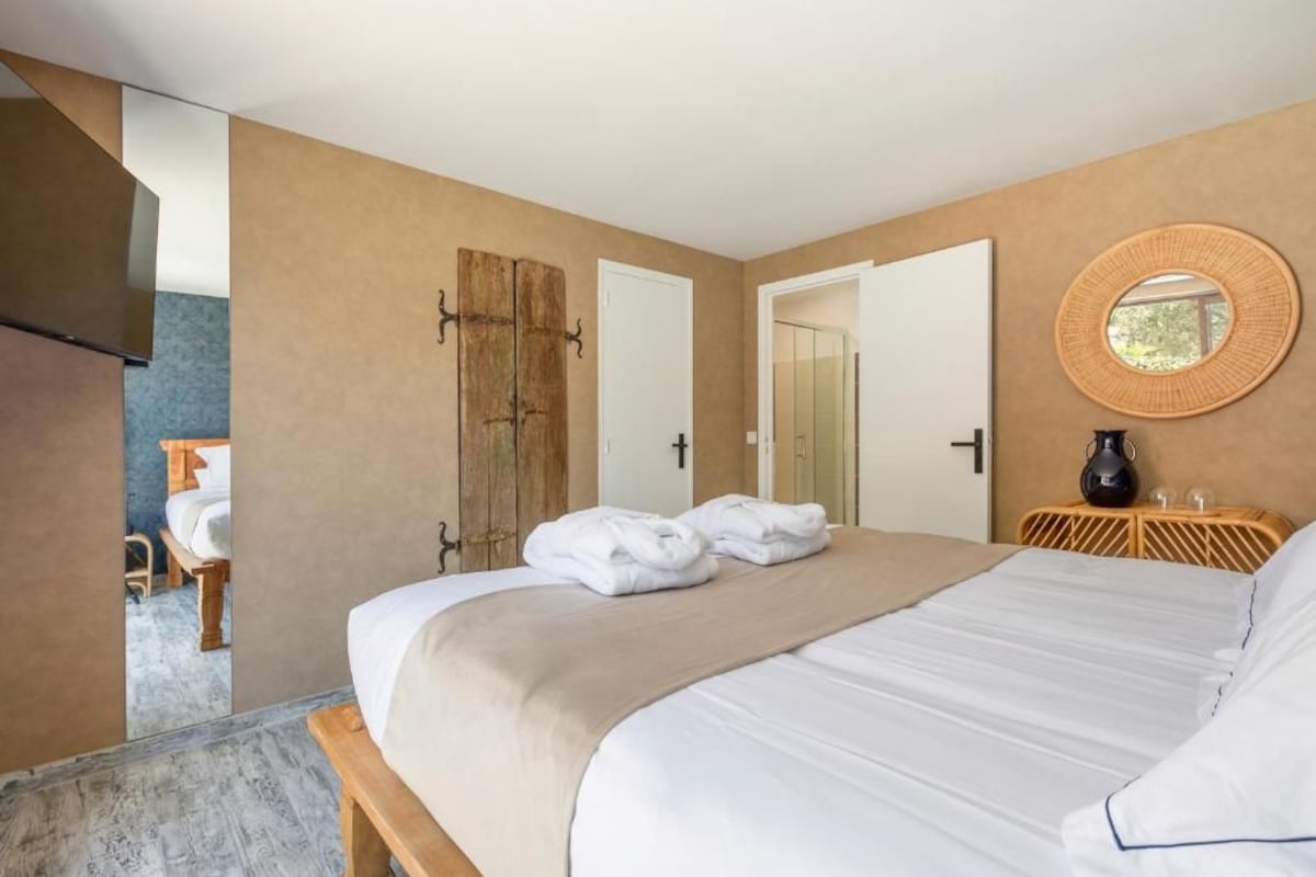 Una habitación de hotel con una cama grande, una puerta de madera, un espejo y una mesita de noche con una lámpara.