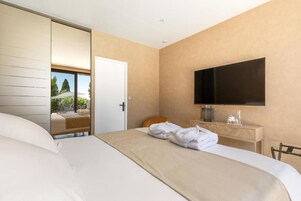 Une chambre d’hôtel comprenant un lit, un téléviseur fixé au mur, une table de chevet en bois et une porte coulissante donnant sur un balcon.