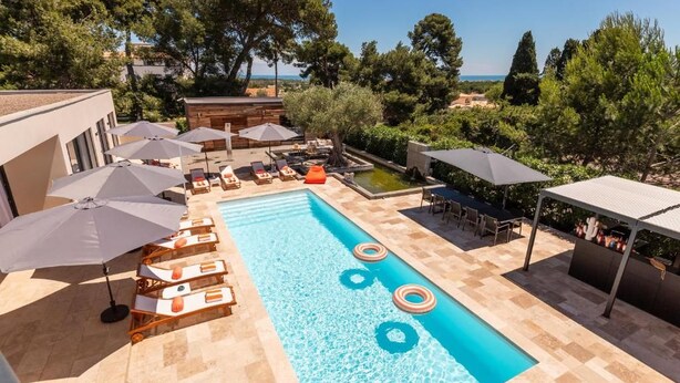 A rectangular swimming pool with lounge chairs and umbrellas, surrounded by trees and a view of the sea. - La Villa Monarque  (Agde)