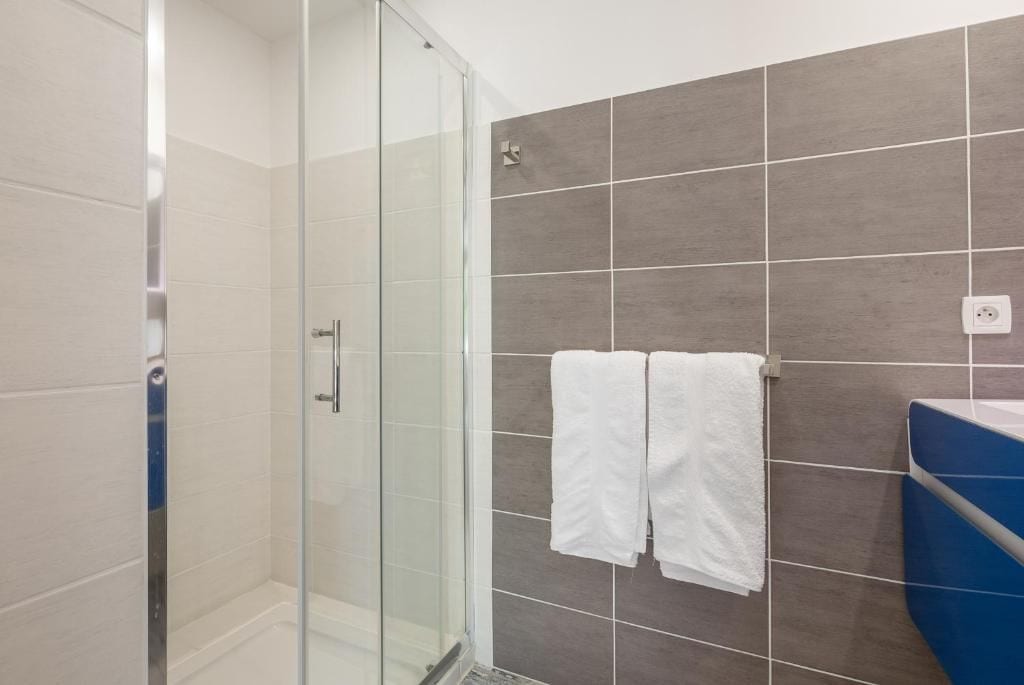 Een badkamer met een glazen douchecabine, betegelde wanden en een blauw aanrecht.