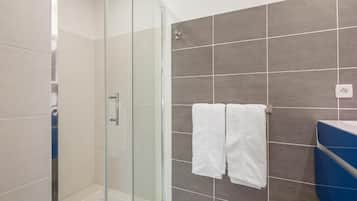 Een badkamer met een glazen douchecabine, betegelde wanden en een blauw aanrecht.