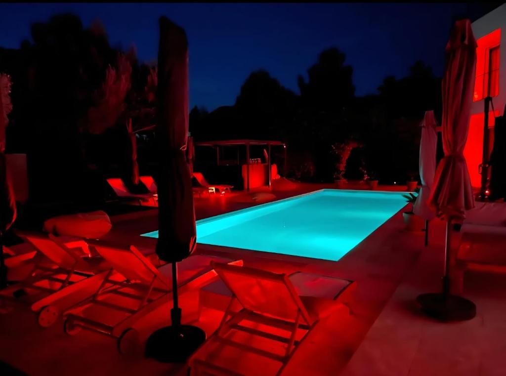 Un espace piscine doté de chaises longues et de parasols, entouré d’arbres.