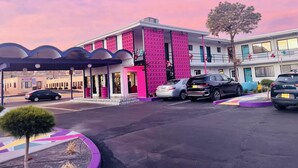 Um edifício com fachada rosa marcante, entrada coberta e estacionamento com vários carros.