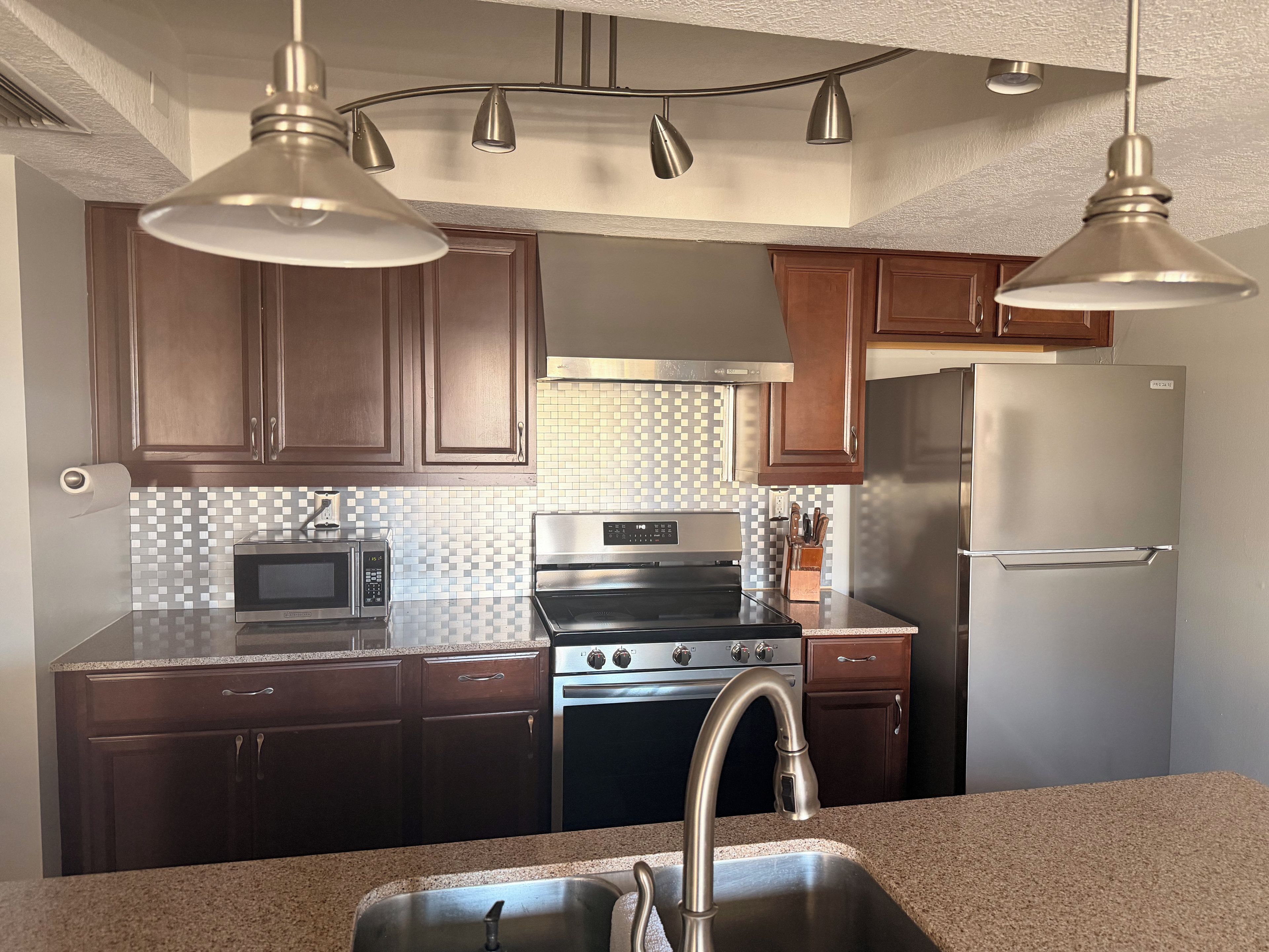 A kitchen with dark wooden cabinets, stainless steel appliances, a granite countertop, and pendant lighting.