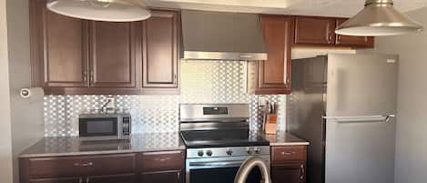 A kitchen with dark wooden cabinets, stainless steel appliances, a granite countertop, and pendant lighting.
