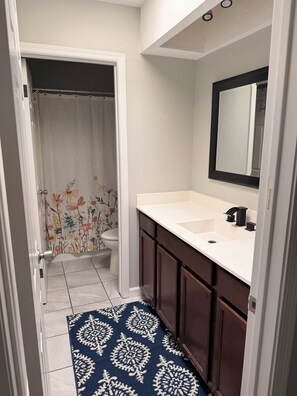 A bathroom with a white sink, dark wooden cabinets, a mirror, and a shower curtain with floral patterns. - Vaulted ceilings, brand new appliances, overlooking pool/hot tub of complex. (Scottsdale)