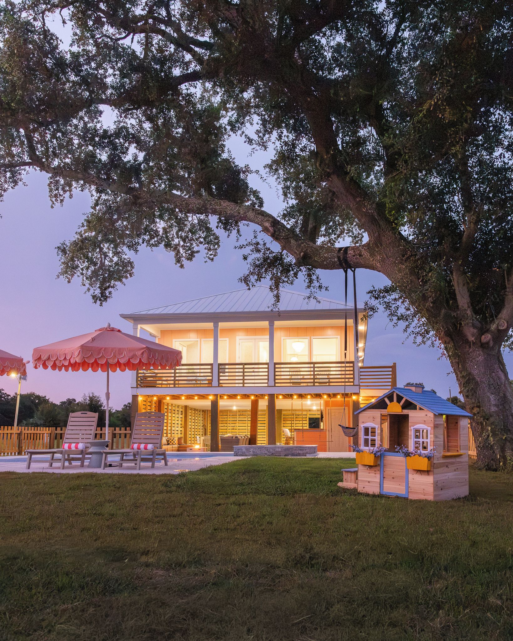 A modern house with a large tree in front, a pool, and outdoor seating.