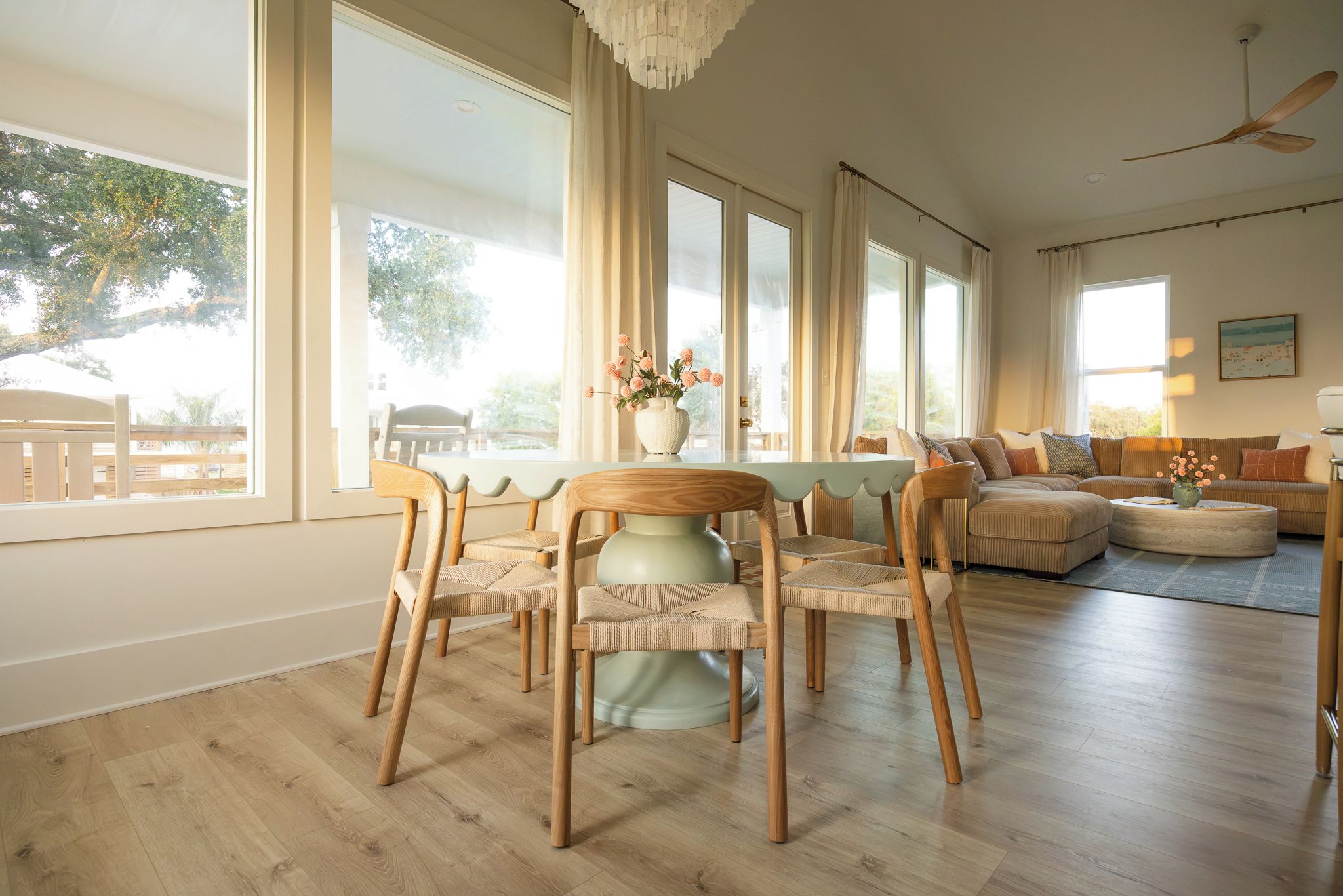 A spacious living room with a large dining table, multiple chairs, a sofa, and a ceiling fan.