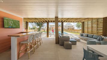 A covered outdoor area with a bar, seating, and a pool.
