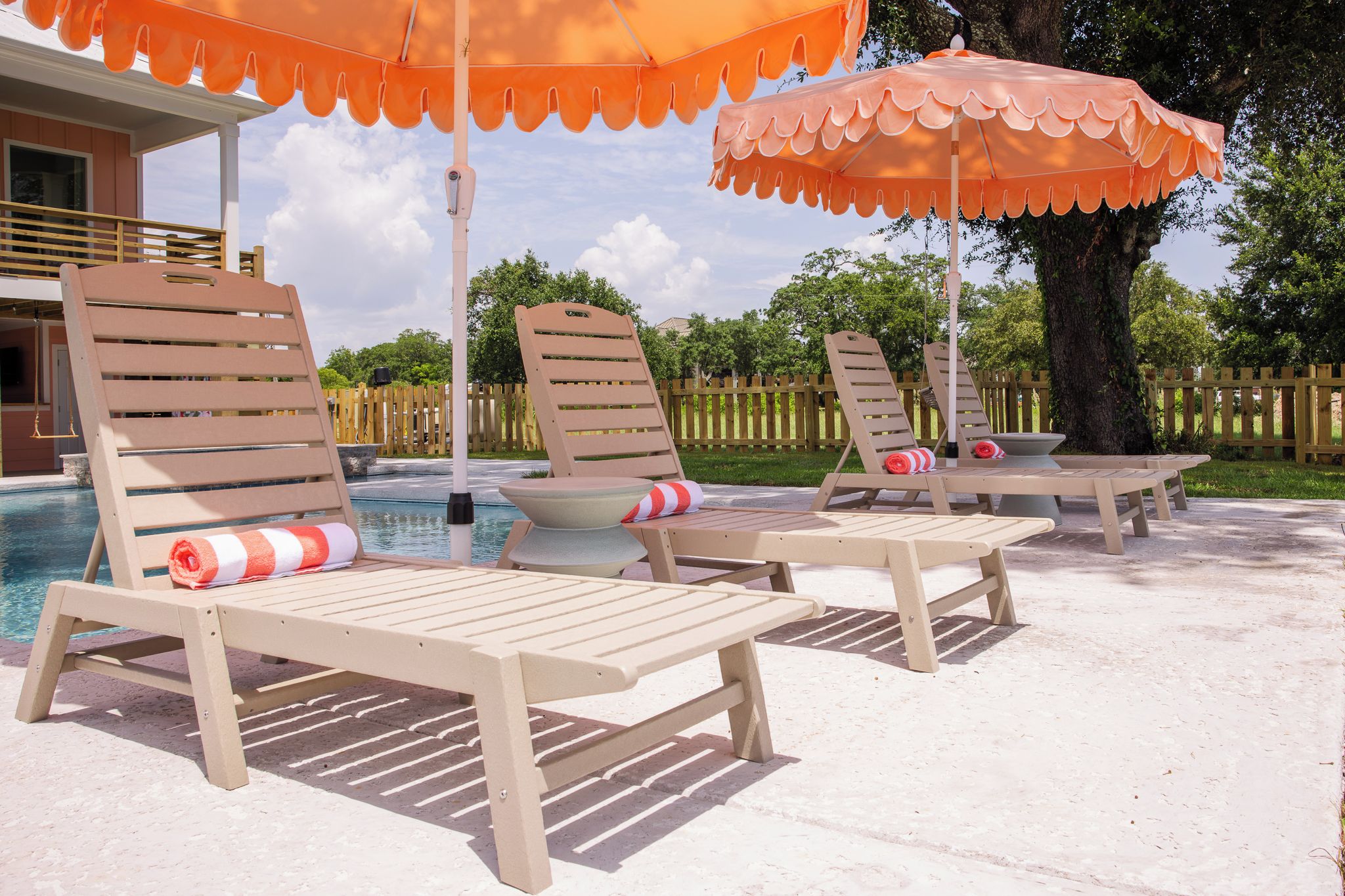 Gemütliche Lounge-Stühle mit Kissen und Sonnenschirmen, ein Pool und ein Holzzaun im Hintergrund.