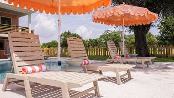 Gemütliche Lounge-Stühle mit Kissen und Sonnenschirmen, ein Pool und ein Holzzaun im Hintergrund.