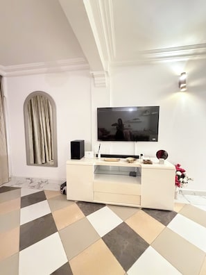 Ein modernes Wohnzimmer mit einem Flachbildfernseher an einer weißen Unterhaltungsanlage, einem gemusterten Boden und einem großen, bogenförmigen Fenster mit Vorhängen.