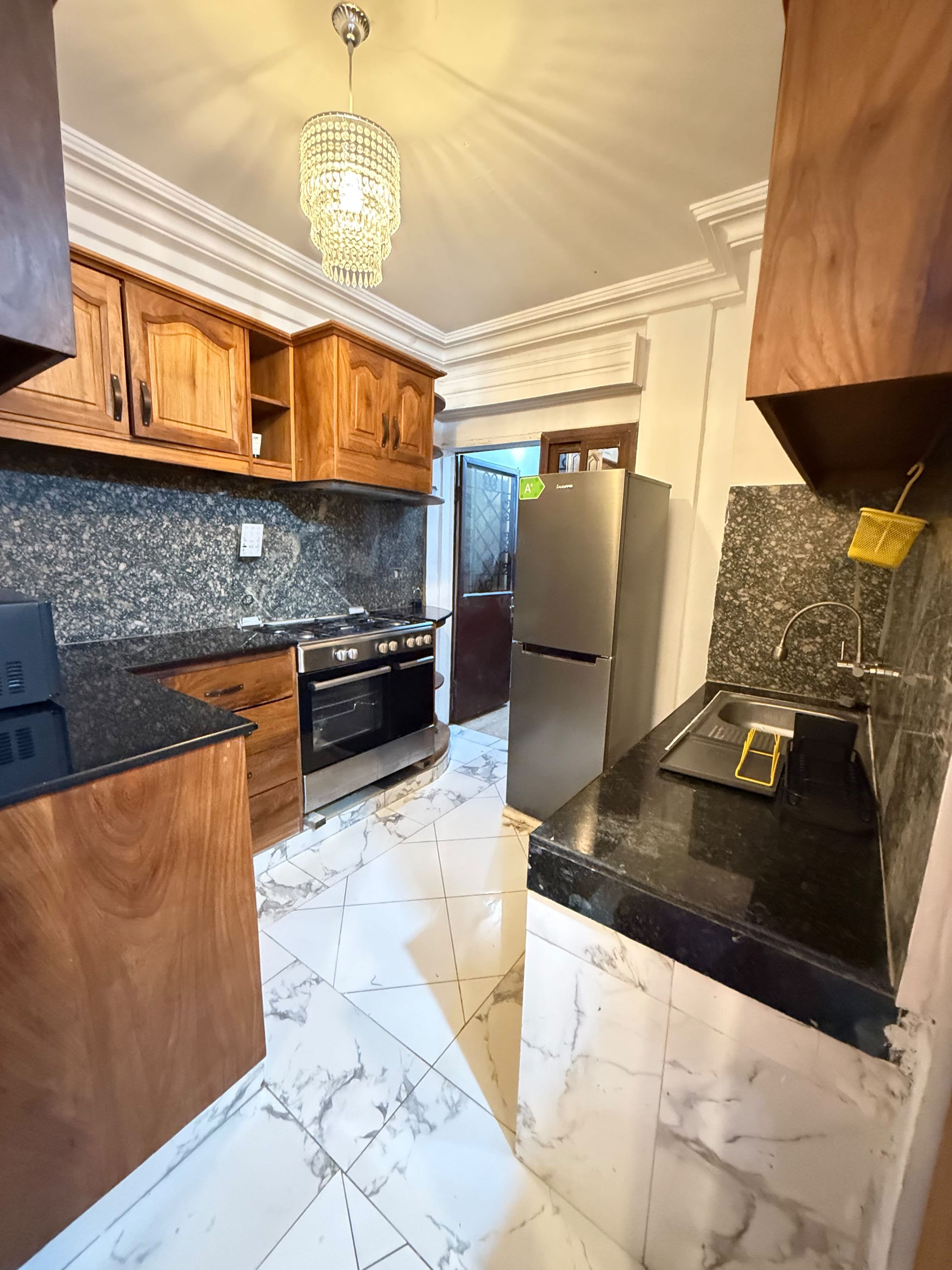 Una cocina con armarios de madera, un refrigerador de acero inoxidable, horno empotrado y piso de mármol.