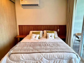 Een hotelkamer met een bed, een houten hoofdeinde, een raam met gordijnen en een airconditioning.