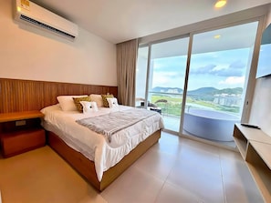A hotel room with a large bed, a wooden headboard, a bedside table, a TV, and a balcony with a view of the city. - Deluxe Suite with Jacuzzi - Pozos Colorados (Magdalena)