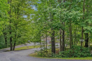A residential area with a road curving through a wooded area, a house with a visible address sign, and a clear sky. - Quechee Art and Trail Retreat (Quechee)