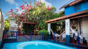 A swimming pool with a wooden deck, surrounded by a fence, and a hammock. - Casa com Piscina e Churrasqueira em Jardim Oceania (João Pessoa)