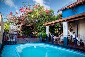 A swimming pool with a wooden deck, surrounded by a fence, and a hammock. - Casa com Piscina e Churrasqueira em Jardim Oceania (João Pessoa)