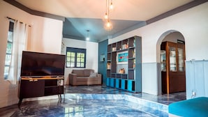 A spacious living room with a flat-screen TV, a sofa, a bookshelf, and a marble floor. - Casa com Piscina e Churrasqueira em Jardim Oceania (João Pessoa)