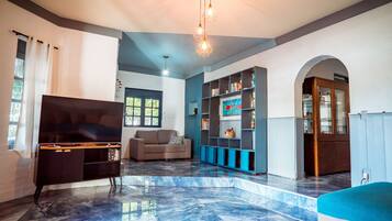 A spacious living room with a flat-screen TV, a sofa, a bookshelf, and a marble floor.