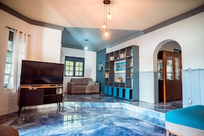 A spacious living room with a flat-screen TV, a sofa, a bookshelf, and a marble floor. - Casa com Piscina e Churrasqueira em Jardim Oceania (João Pessoa)