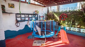 Área de recreação infantil com um trampolim, escorrega e decorações nas paredes.