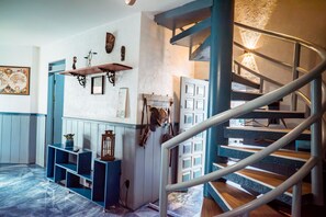 Escada em espiral com corrimão de metal, prateleira fixa na parede com objetos decorativos e mesa consola azul com um vaso.