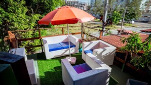 An outdoor seating area with wicker furniture and a red umbrella. - Casa com Piscina e Churrasqueira em Jardim Oceania (João Pessoa)