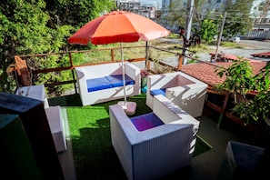 An outdoor seating area with wicker furniture and a red umbrella. - Casa com Piscina e Churrasqueira em Jardim Oceania (João Pessoa)