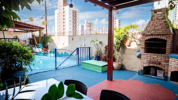 An outdoor patio with a pool, a brick oven, and potted plants. - Casa com Piscina e Churrasqueira em Jardim Oceania (João Pessoa)
