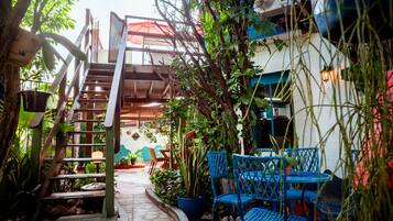 A narrow outdoor pathway leading to a seating area with blue chairs and potted plants.