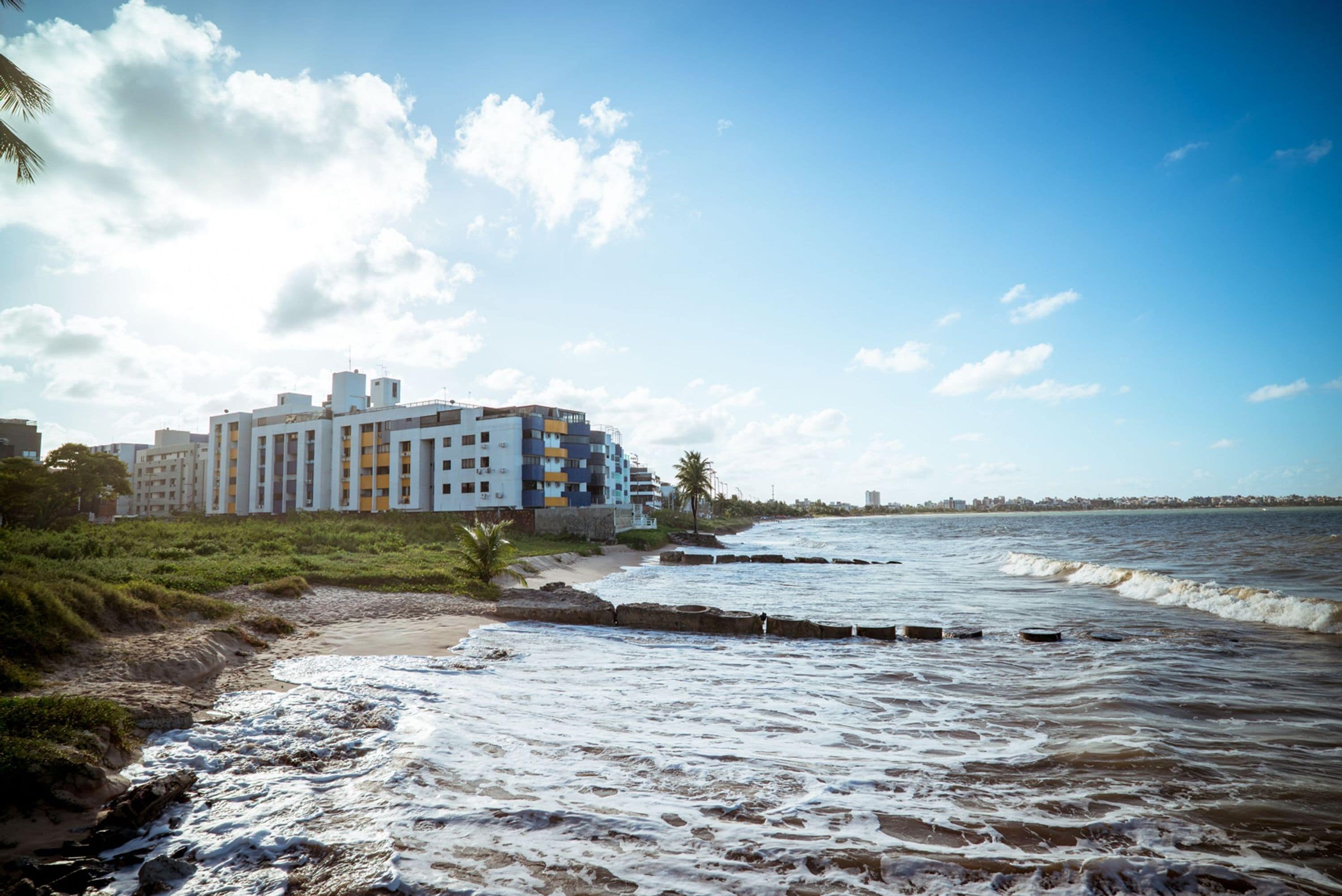 A coastal hotel with a beachfront view, a sandy beach, and a rocky shoreline.