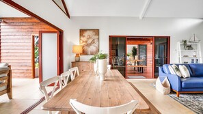 A spacious living area with a wooden dining table, white chairs, a blue sofa, and a large painting on the wall. - Casa Jana - Kurrimine Beach (Kurrimine Beach)