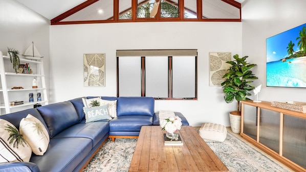 A living room with a blue sofa, a coffee table, a bookshelf, and a large window.