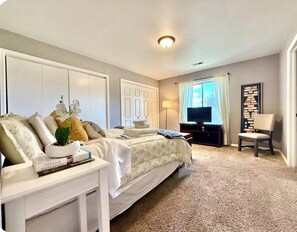 Ein Schlafzimmer mit Bett, Nachttisch, Fernseher, Sessel und Bücherregal.
