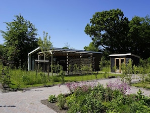 Ein modernes Gebäude mit einer überdachten Terrasse, umgeben von üppigem Grün und einem gepflasterten Weg.