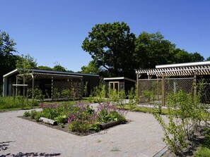 A garden with a brick pathway, wooden pergolas, and a variety of plants. - Luxury Holiday Home Surrounded by Water and Forest (Sint Nicolaasga)