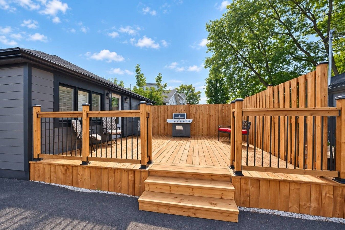 Une terrasse en bois avec un barbecue et un espace salon, le tout entouré d’une clôture en bois.