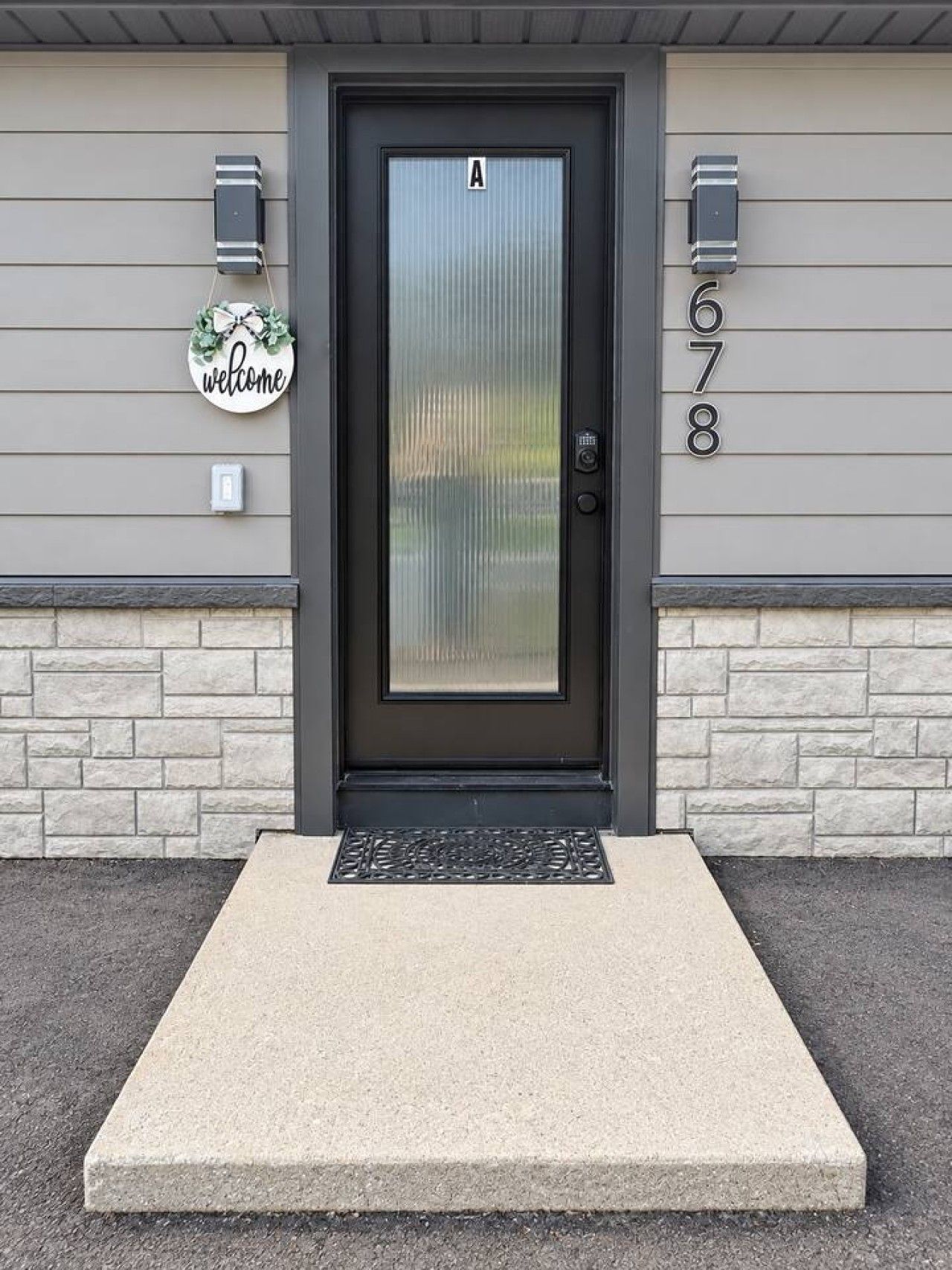 A modern house with a dark grey door, a welcome sign, and a mailbox.