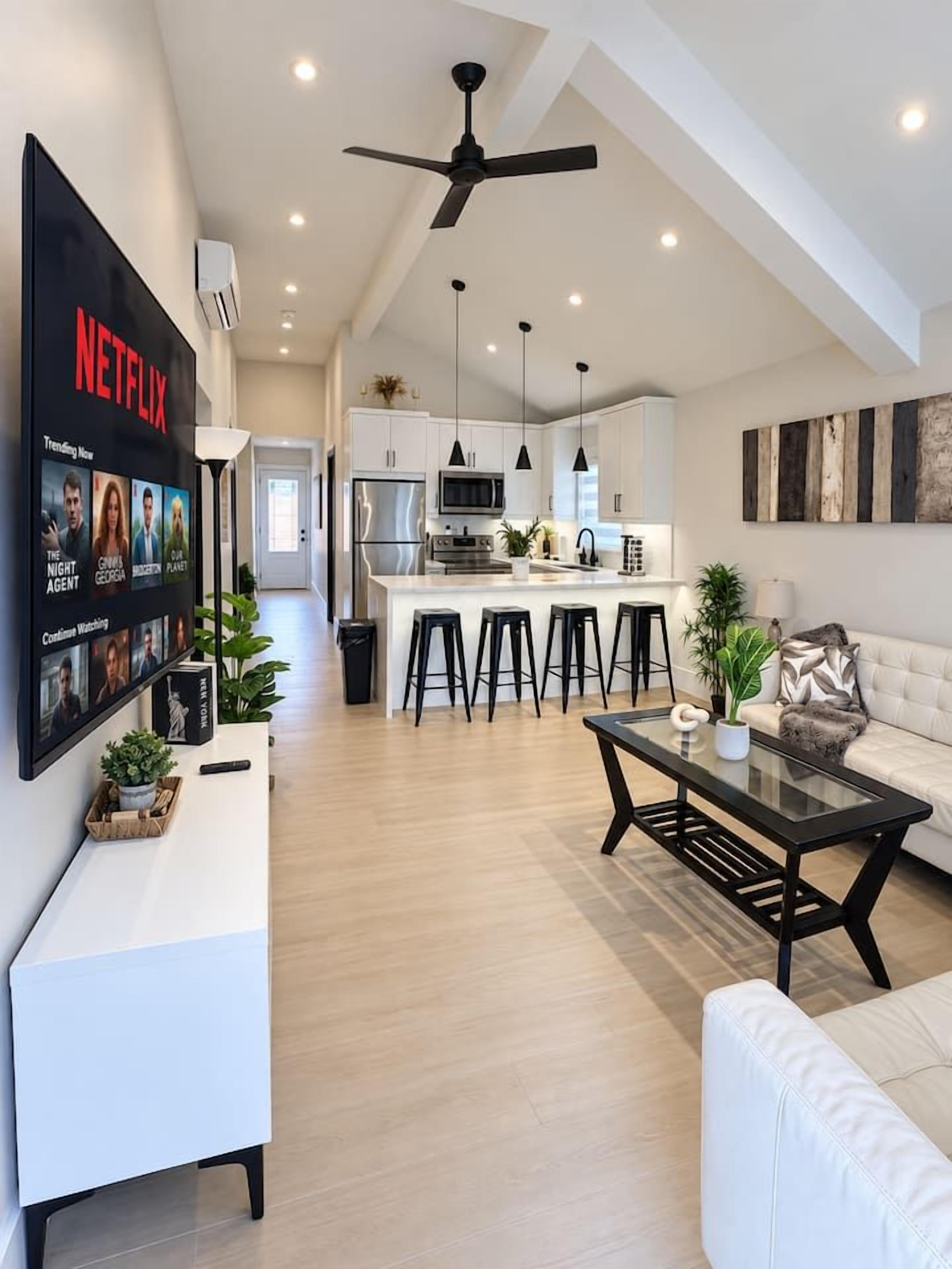 Una sala de estar moderna con un sofá, una mesa de centro y un televisor en la pared mostrando un anuncio de Netflix.