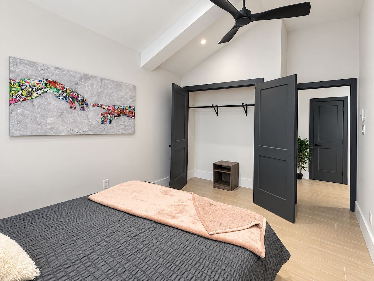 A modern bedroom with a bed, a ceiling fan, a gray textured wall, and a colorful abstract painting.