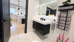 Un baño moderno con inodoro blanco, tocador negro, espejo grande y un perchero para toallas.