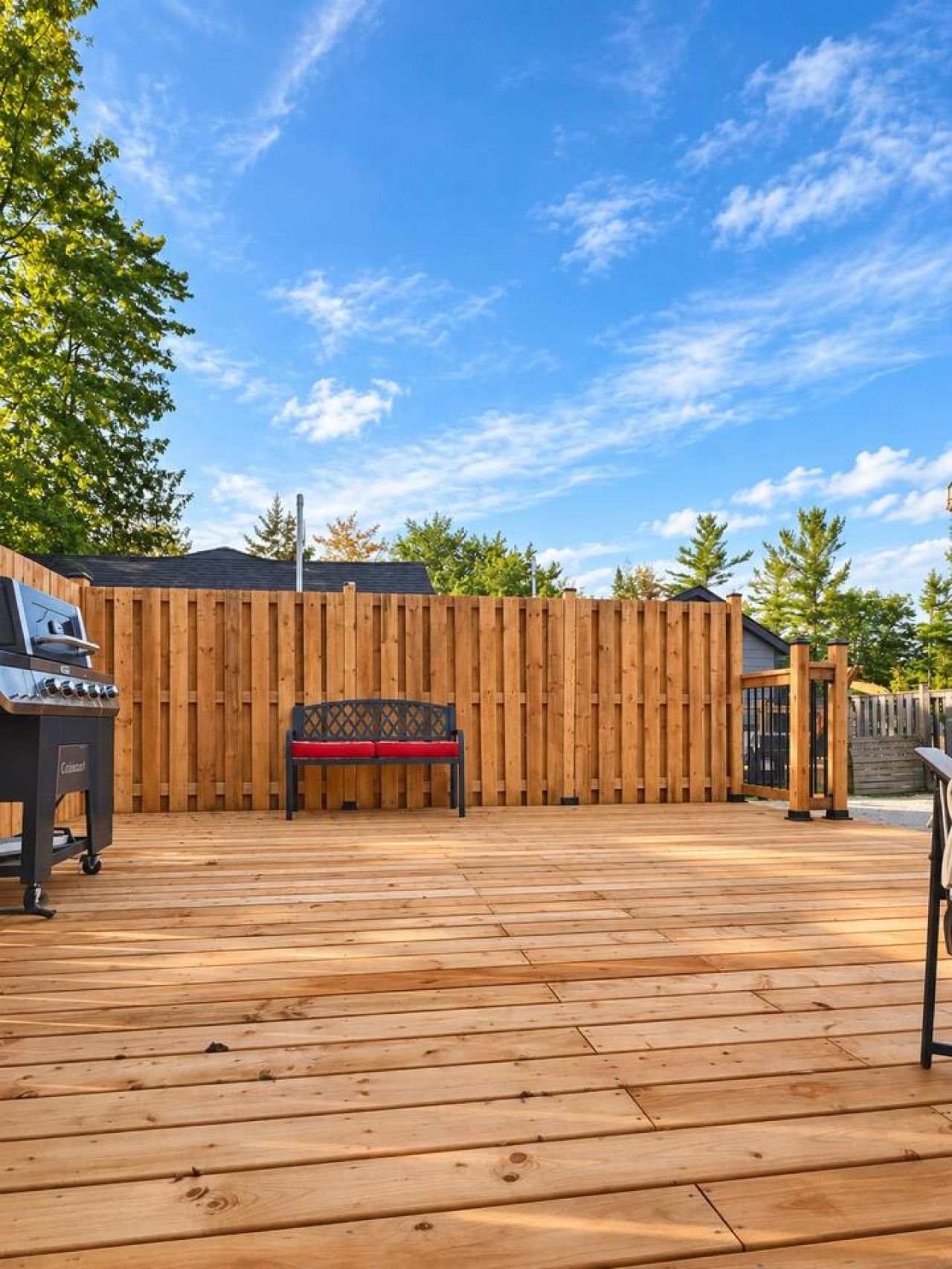 A wooden deck with a barbecue grill, a bench, and a wooden fence.