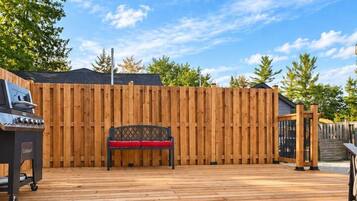 A wooden deck with a barbecue grill, a bench, and a wooden fence.