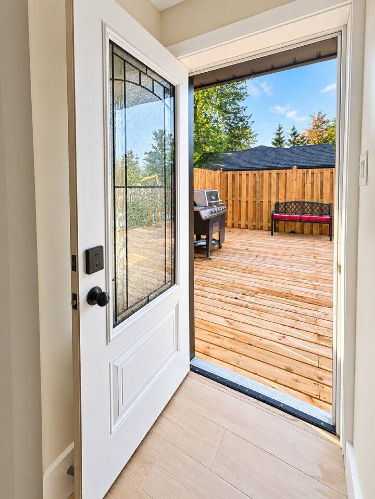 A door leading to a wooden deck with a barbecue grill and a bench.